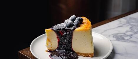 A slice of cheesecake with blueberries on a white plate on a marble surface.