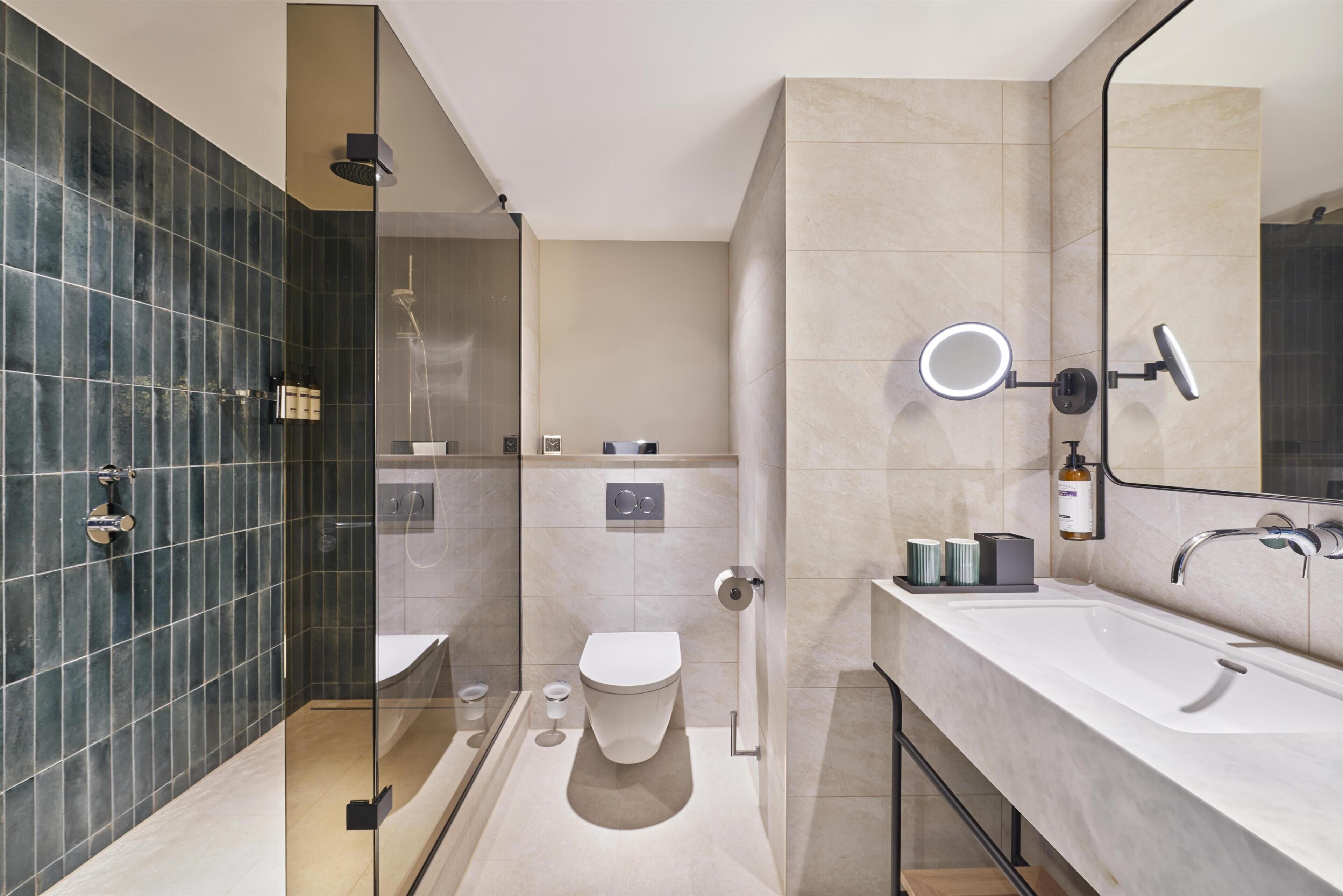 Een moderne badkamer met een douchecabine, toilet, wastafel en spiegel.