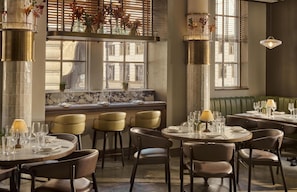 A restaurant interior with round tables, chairs, and a green booth seating area. - Hyatt Regency London Blackfriars (London)
