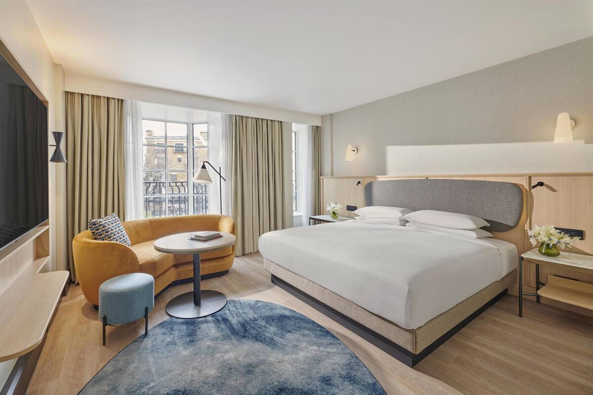 Une chambre d’hôtel avec un grand lit, un canapé, une petite table ronde et une vue sur la ville par la fenêtre.