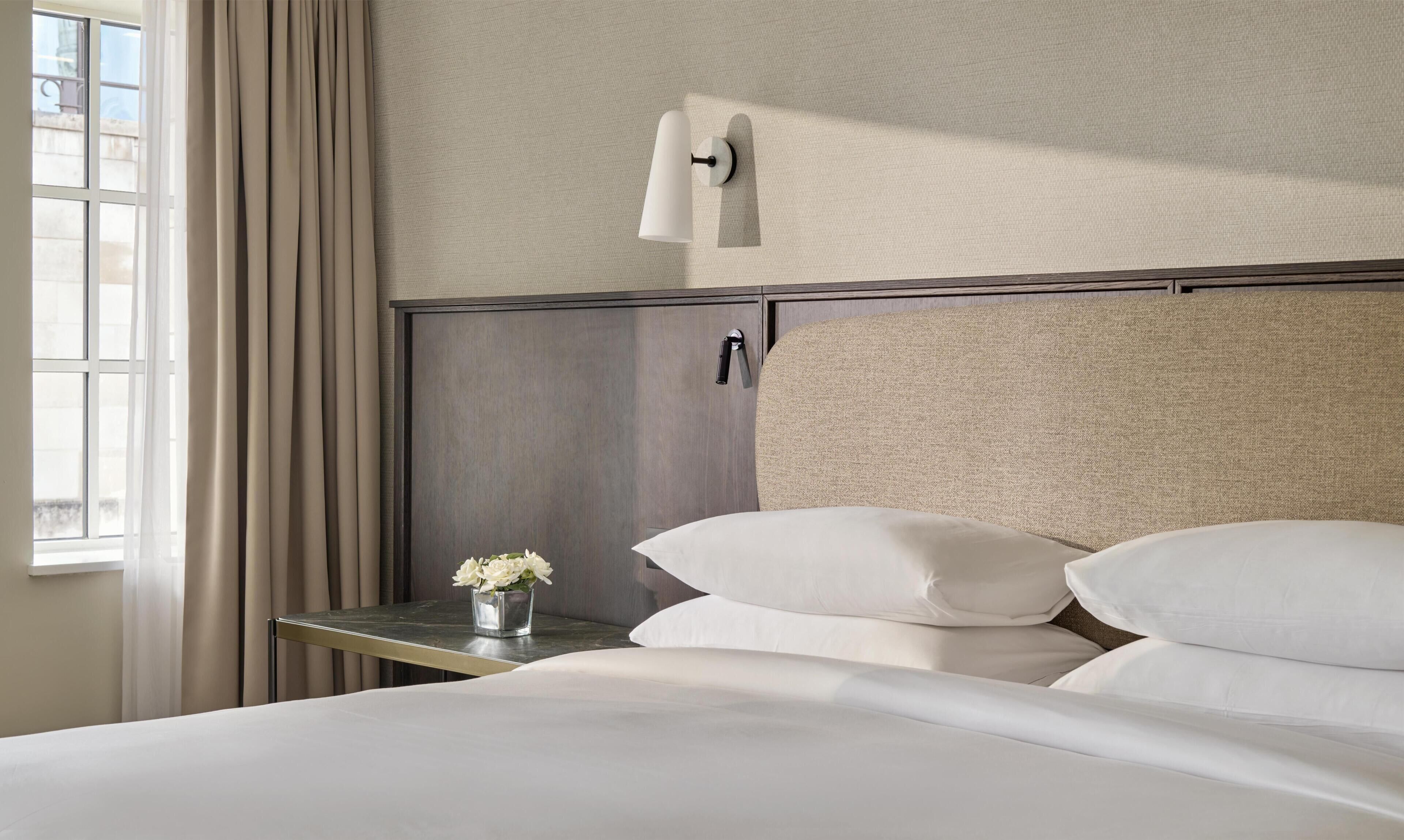 A hotel room with a bed, a nightstand, a lamp, and a window with curtains.