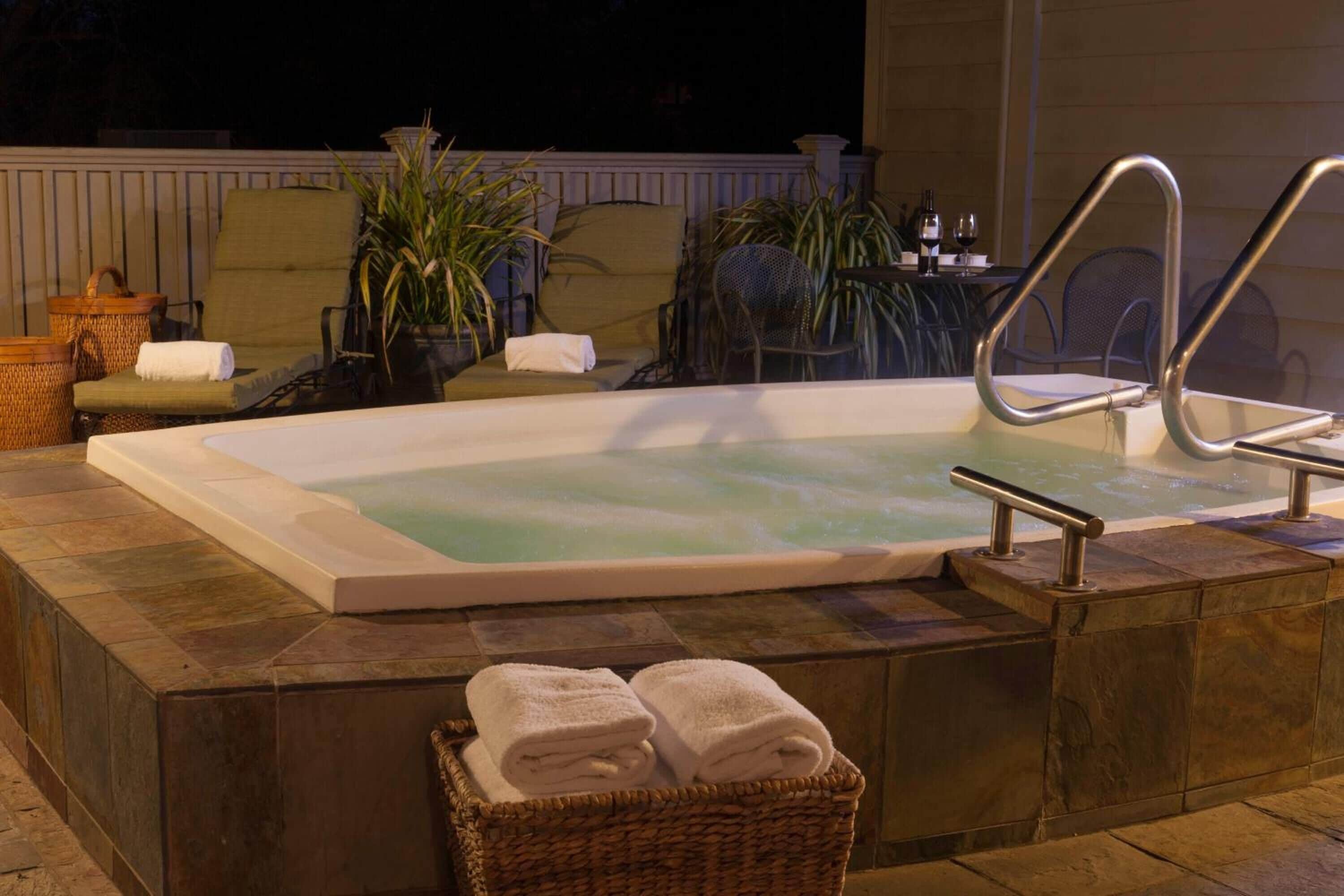 A hot tub with a metal railing, surrounded by lounge chairs and potted plants.