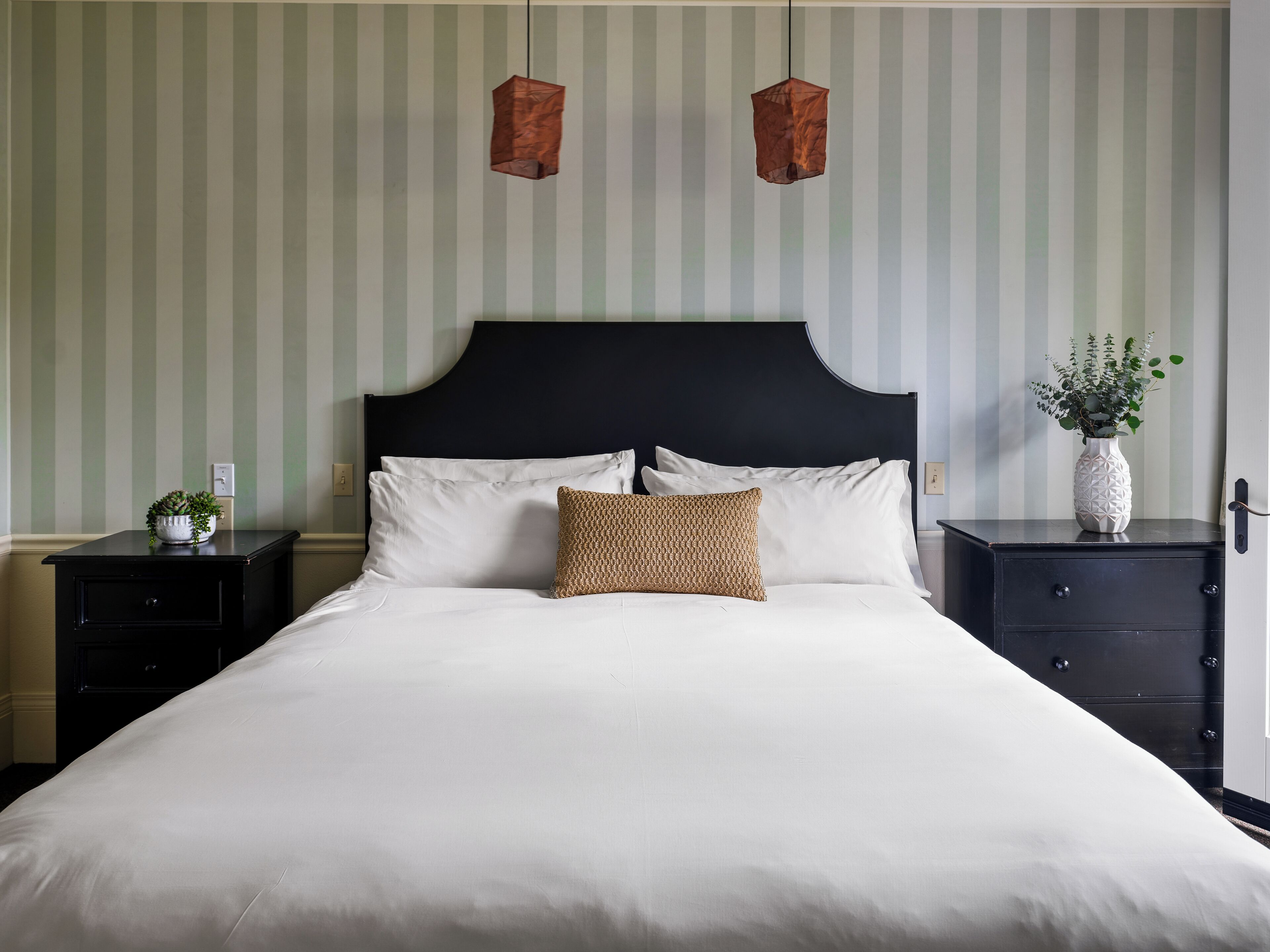 A neatly made bed with white linens, a dark headboard, and a single decorative pillow.