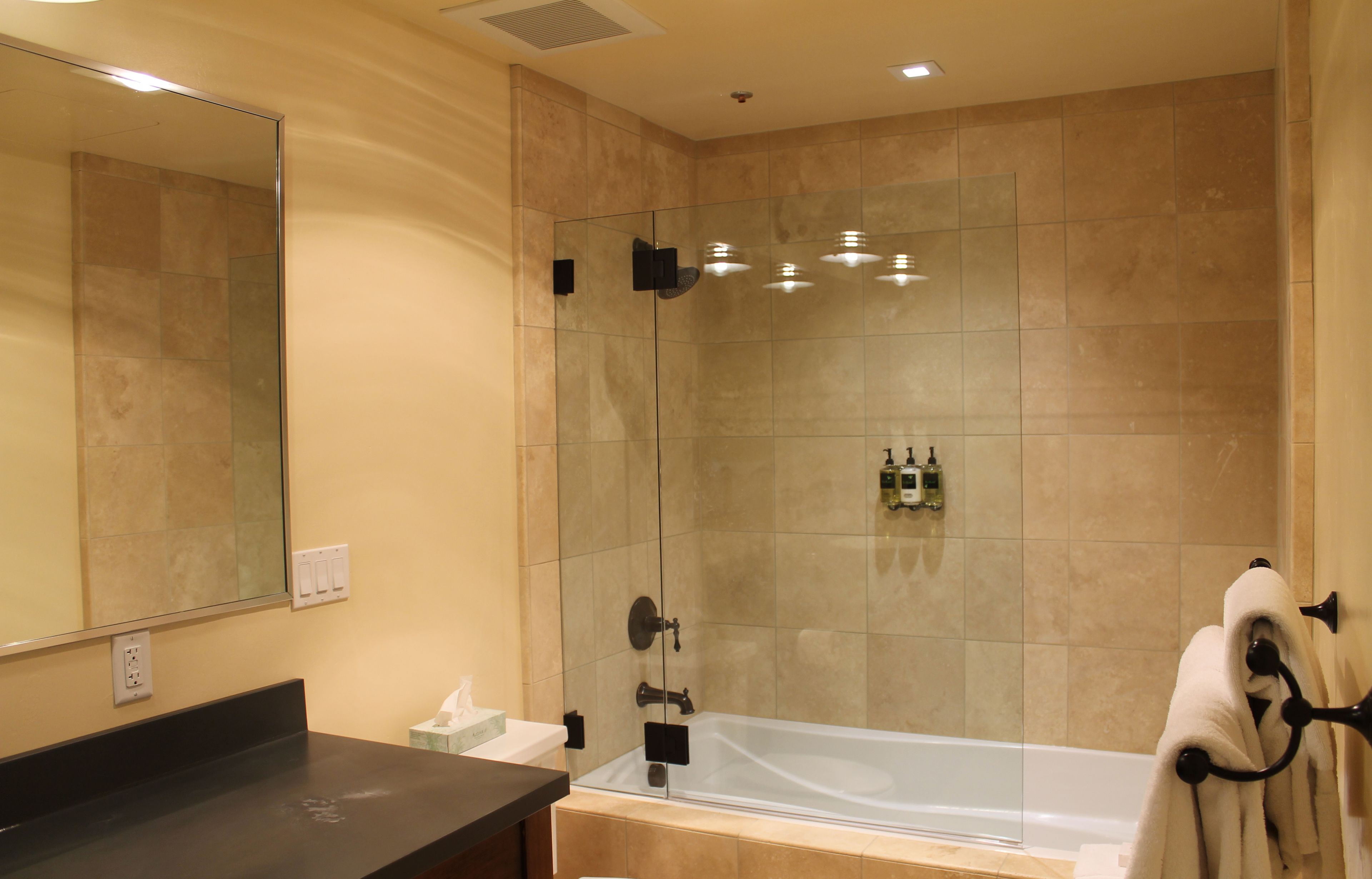 A modern bathroom with a glass-enclosed shower, a large mirror, a bathtub, and a towel rack.
