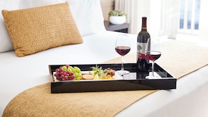 A neatly arranged breakfast tray with grapes, cheese, and a bottle of wine on a bed with white bedding and a brown pillow. - Inn At Sonoma - A Four Sisters Inn (Sonoma)