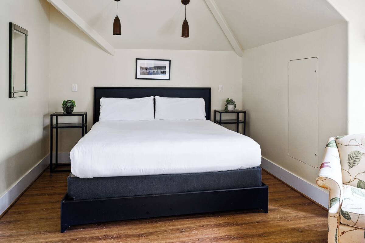 A bedroom with a bed, two bedside tables, a framed picture, and a ceiling light fixture.