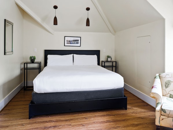Un dormitorio con cama, dos mesitas de noche, un cuadro enmarcado y una lámpara en el techo.