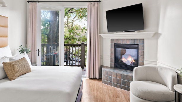 A hotel room with a bed, a seating area with a chair, a fireplace, and a television mounted above it. - Inn At Sonoma - A Four Sisters Inn (Sonoma)