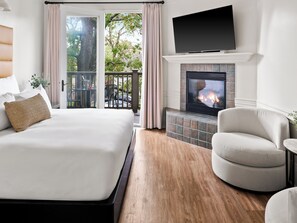 Una habitación de hotel con cama, zona de estar con una silla, chimenea y televisor montado arriba.