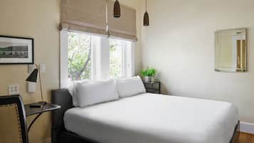 A bedroom with a bed, bedside tables, a chair, a lamp, a potted plant, and a window with a view of trees.