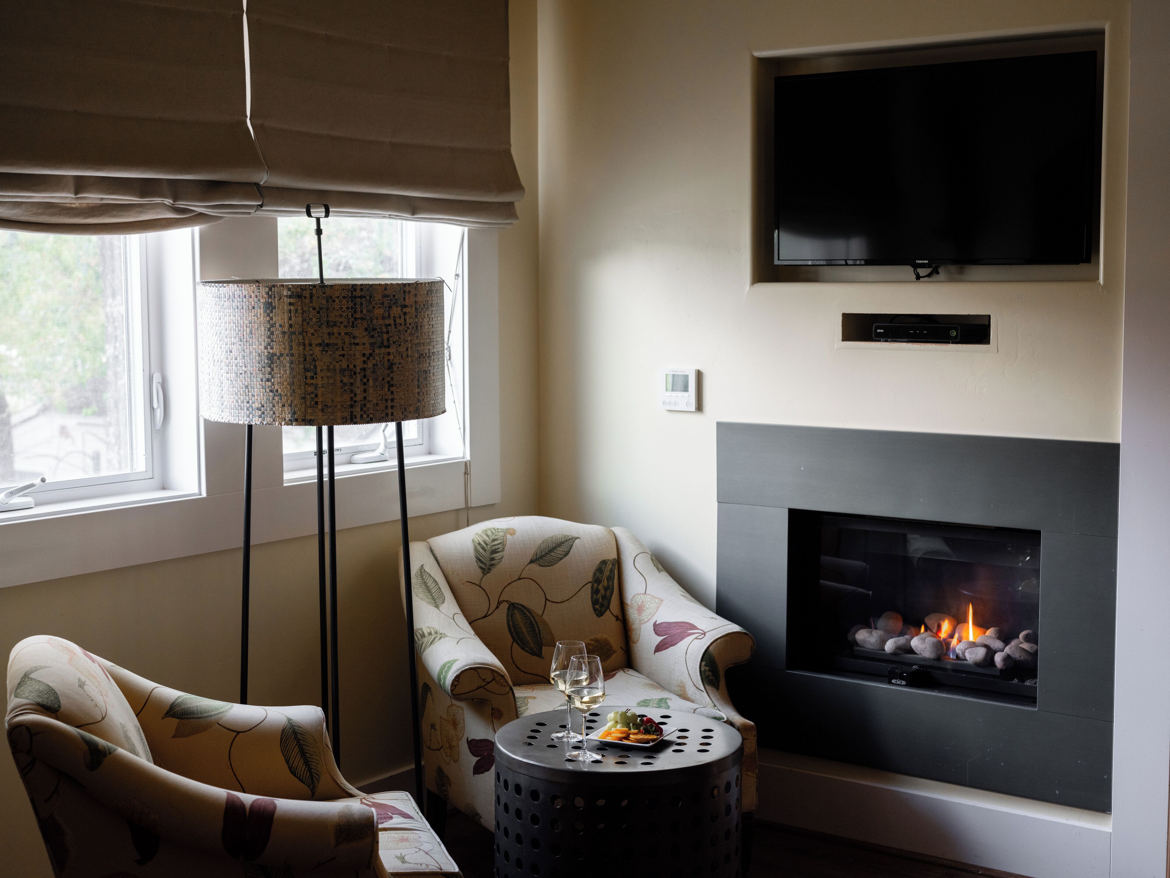 Una sala de estar con chimenea, televisor montado en la pared y un sillón estampado.