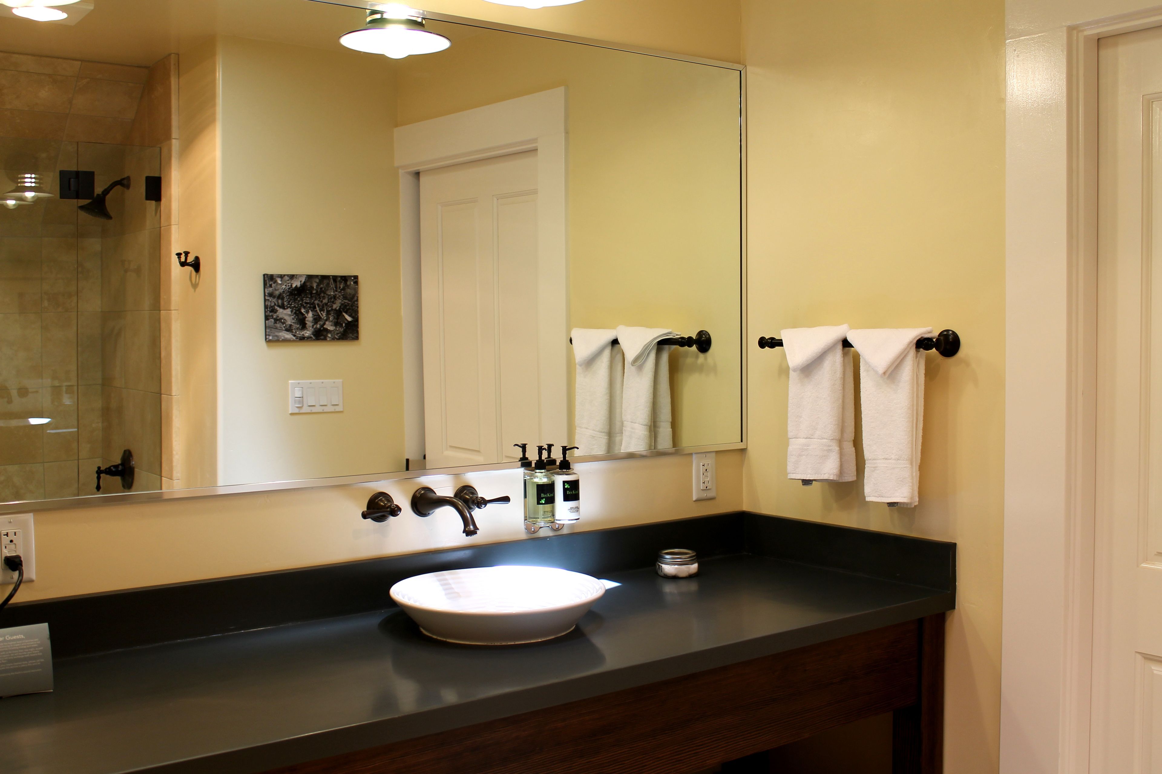 A bathroom with a large mirror, a sink, and two towel racks.