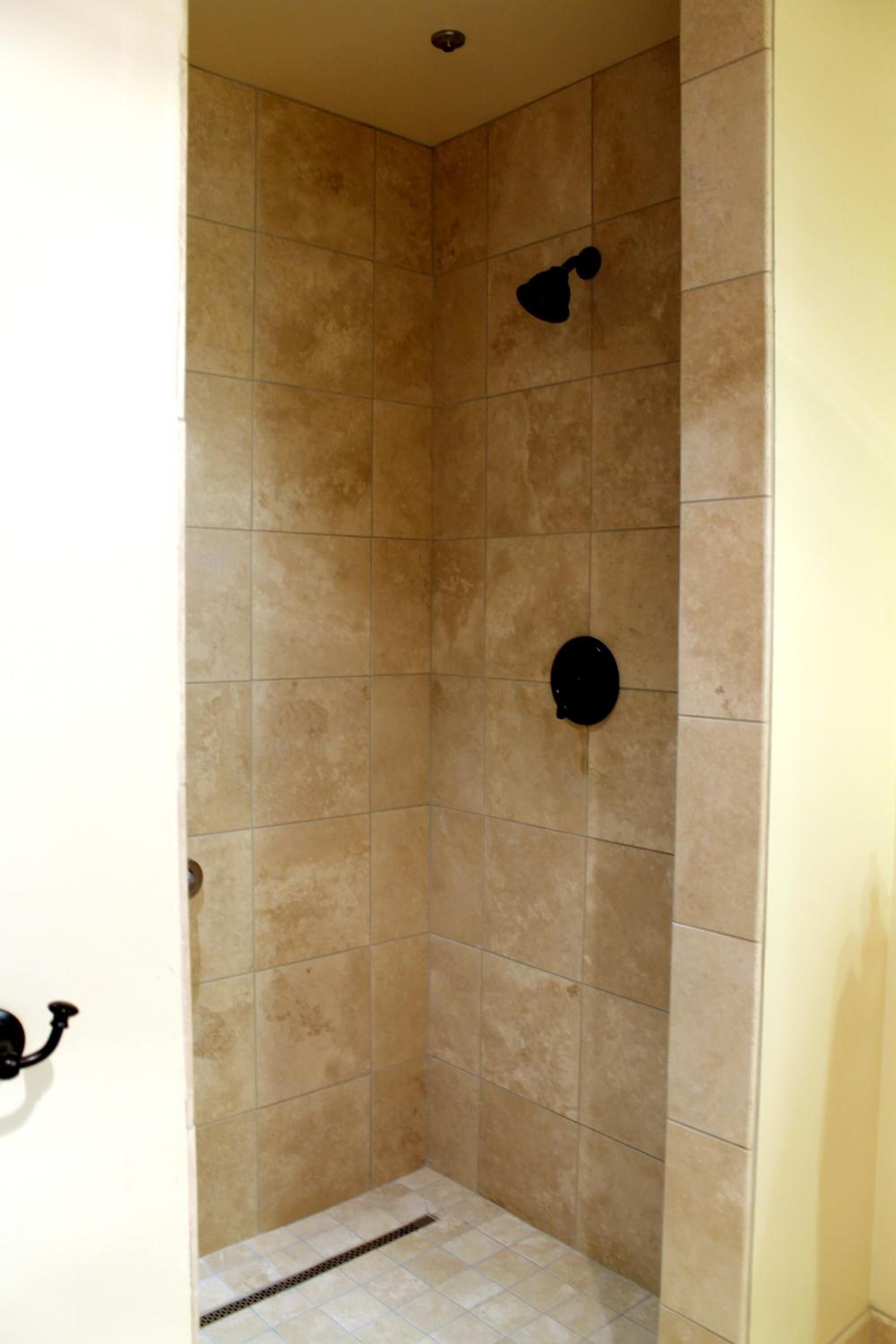 A tiled shower stall with a wall-mounted showerhead and a floor drain.