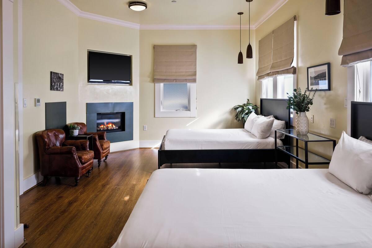 A modern bedroom with a fireplace, two beds, a sofa, and a dining table.