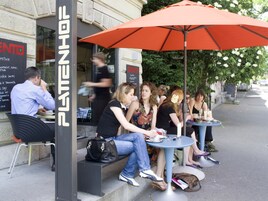 An outdoor cafe with tables and chairs under an orange umbrella.