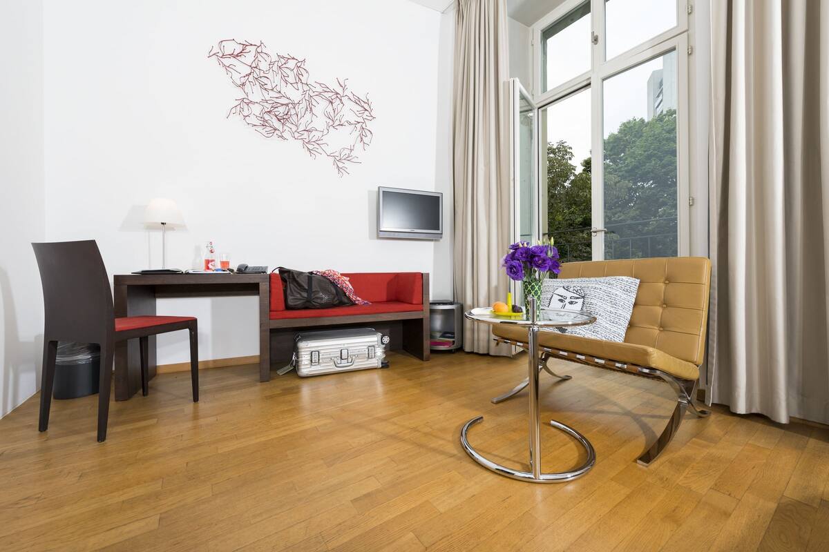 Una sala de estar moderna con un sofá rojo, un sillón marrón, un escritorio y un televisor en la pared.