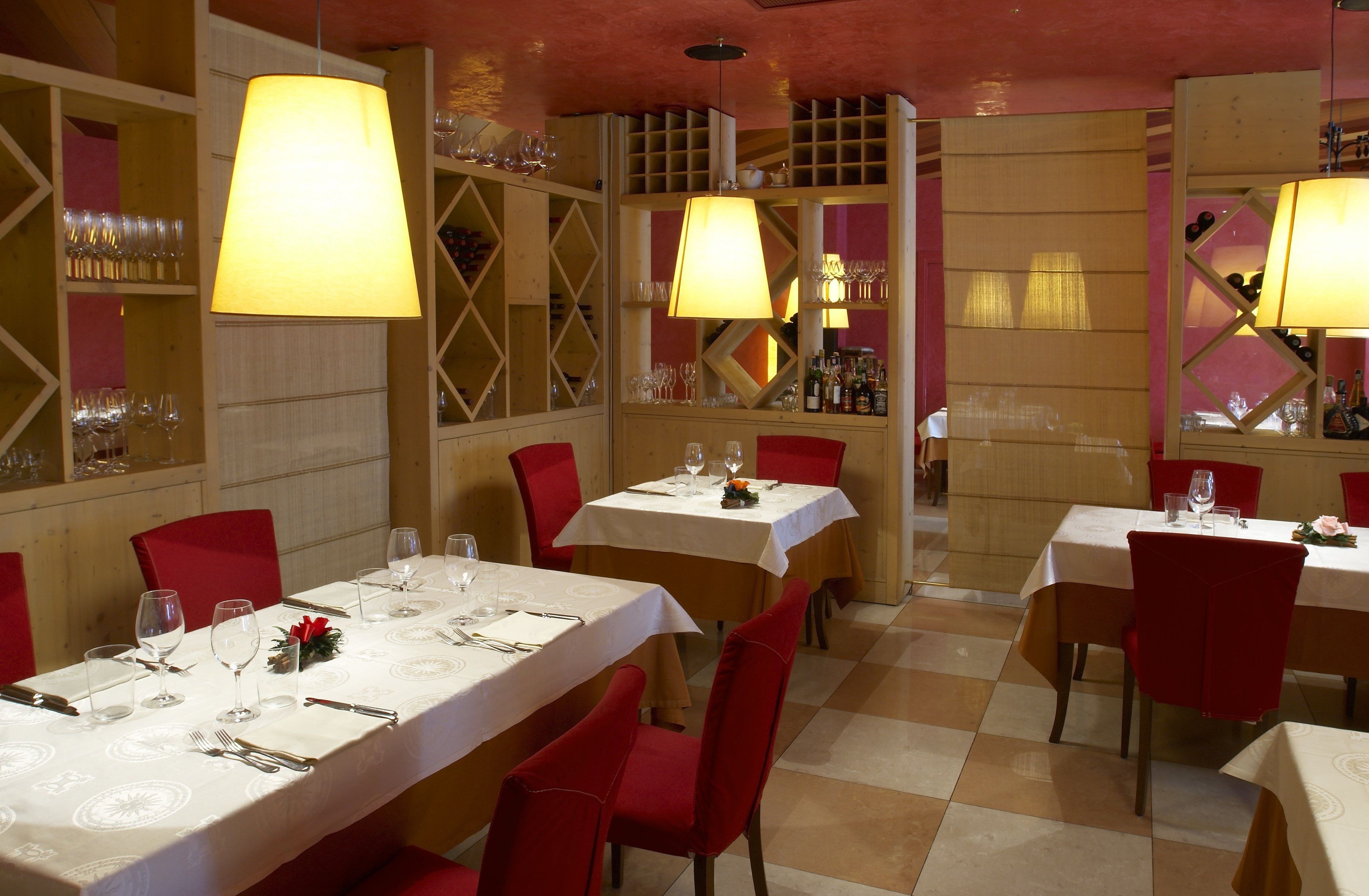 A restaurant with multiple tables set for dining, each with a white tablecloth and red chairs.