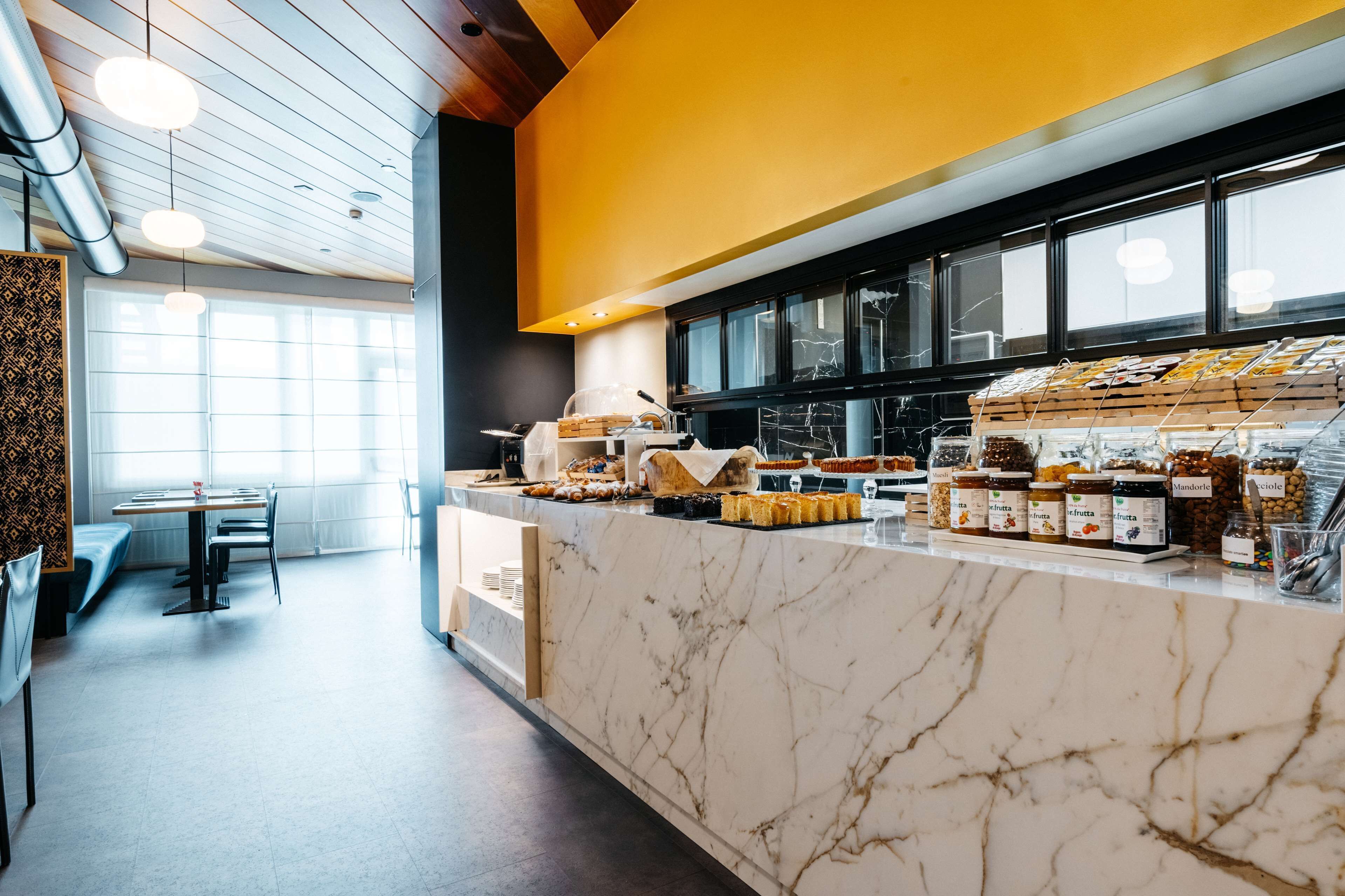 A modern cafe with marble countertops, a variety of baked goods, and a seating area with tables and chairs.