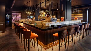 Eine Bar mit einer langen Theke, mehreren Hockern und einem Barkeeper.