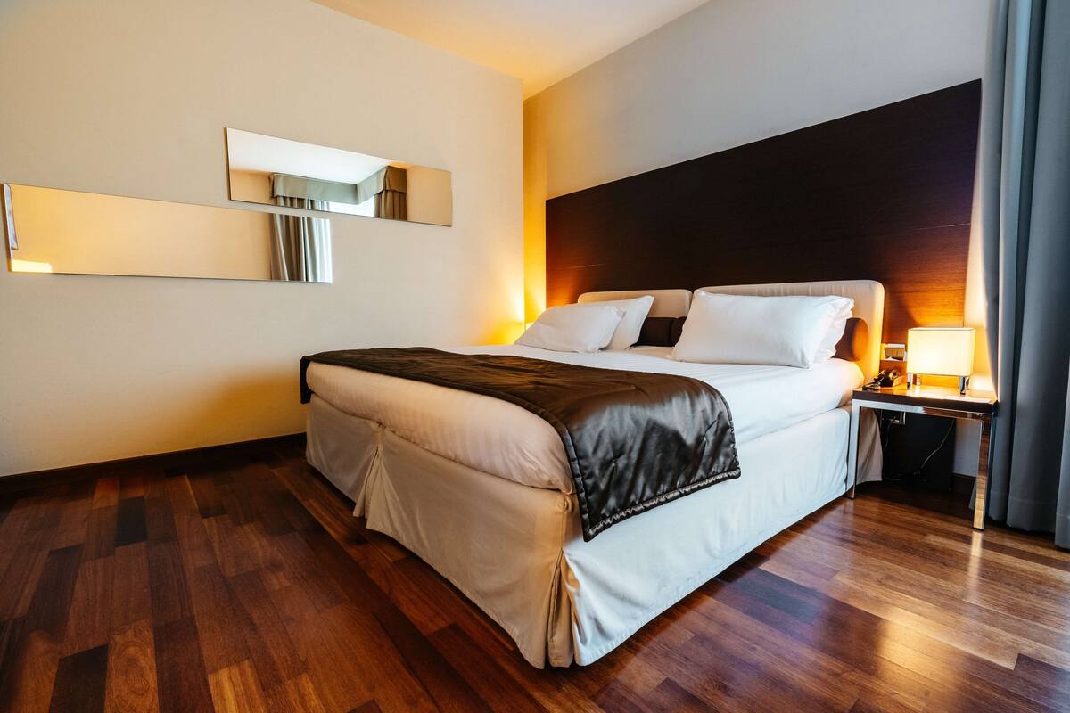 Una habitación de hotel moderna con una cama grande, una mesita de noche, un espejo y suelo de madera.