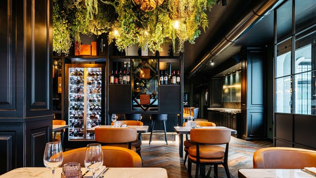 Ein Restaurant mit Marmortischen, Ledersesseln, einem Weinkühlschrank und hängenden Pflanzen.