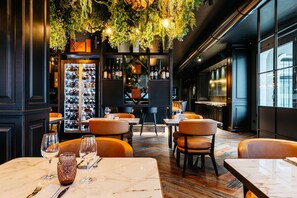 L’intérieur d’un restaurant avec des tables en marbre, des fauteuils en cuir, un réfrigérateur à vin et des plantes suspendues.