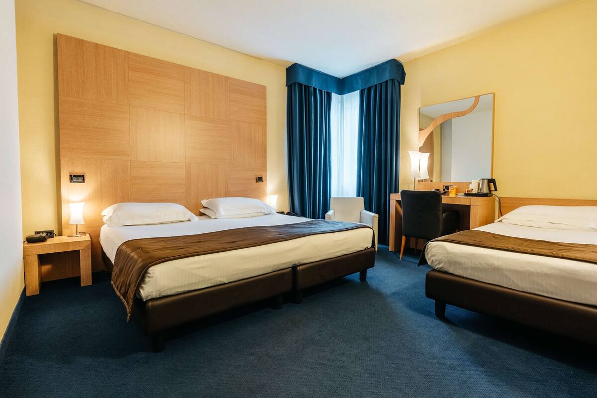 Una habitación de hotel con dos camas, un escritorio, una silla y un espejo grande.