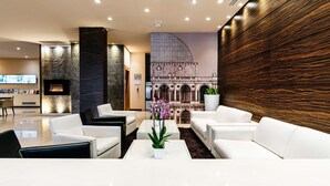 Eine moderne Lobby mit weißen Sofas, einem Kamin und einem großflächigen Wandbild eines Gebäudes.