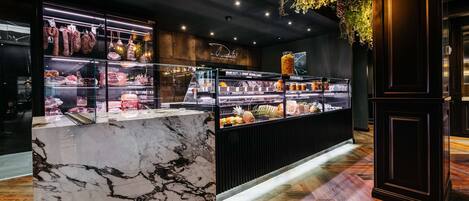 A modern deli counter with glass display cases, a marble countertop, and a hanging plant.
