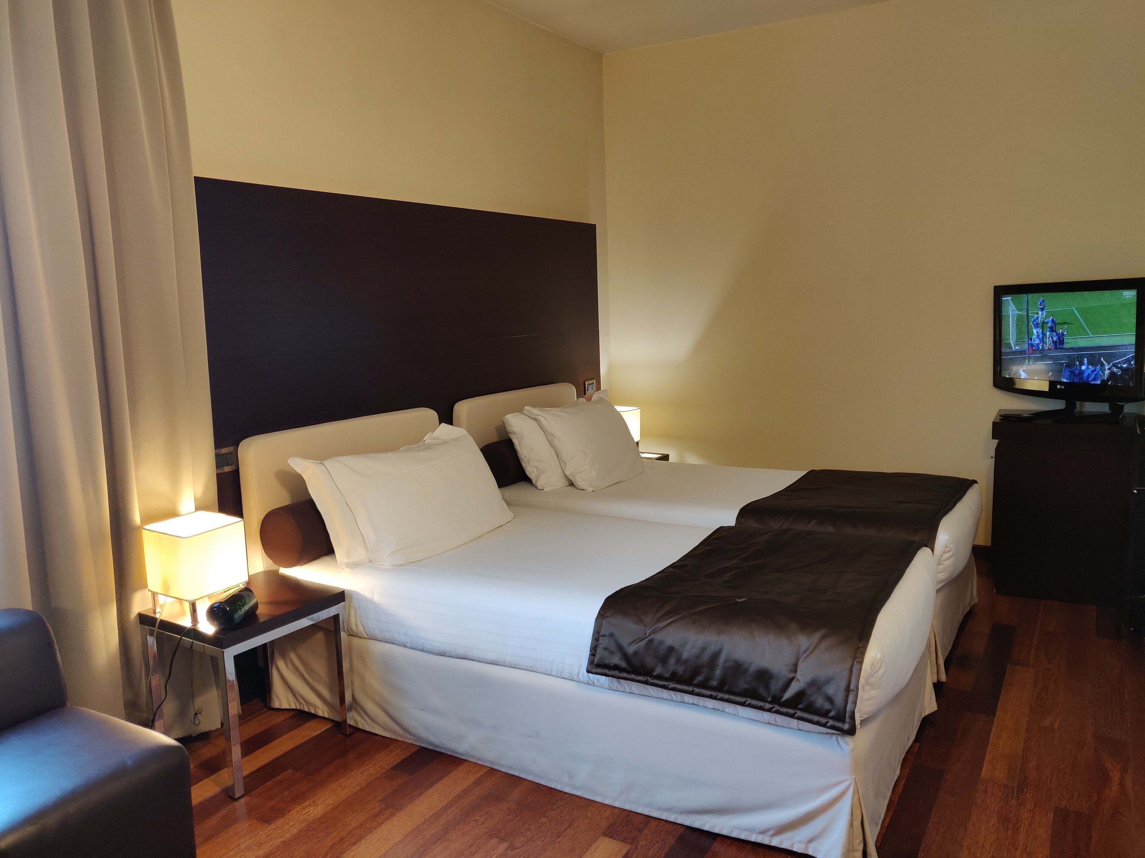 Una habitación de hotel con cama, mesitas de noche, televisor y lámpara.