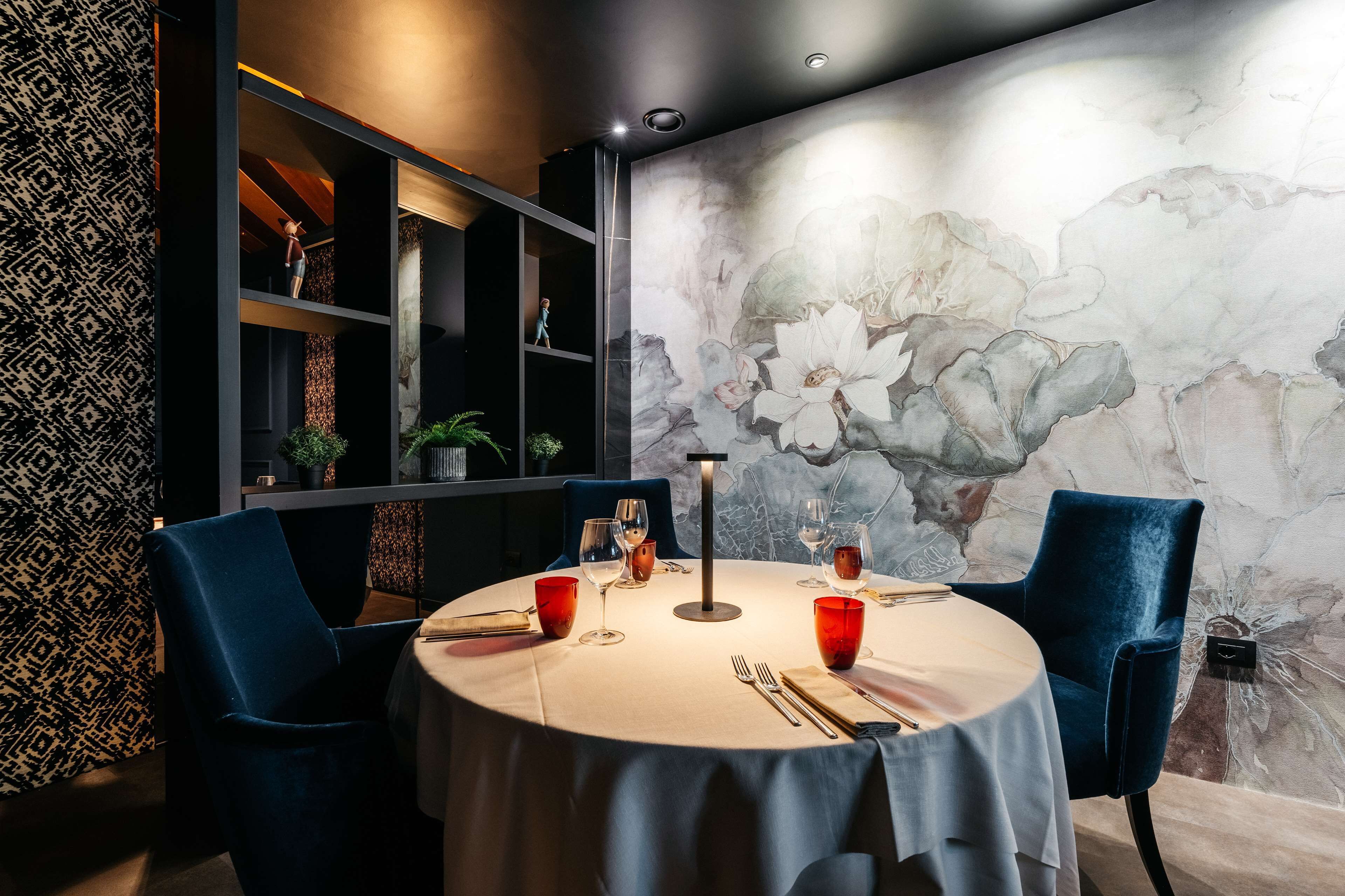 A dining area with a round table, two blue chairs, and a wall with a floral mural.