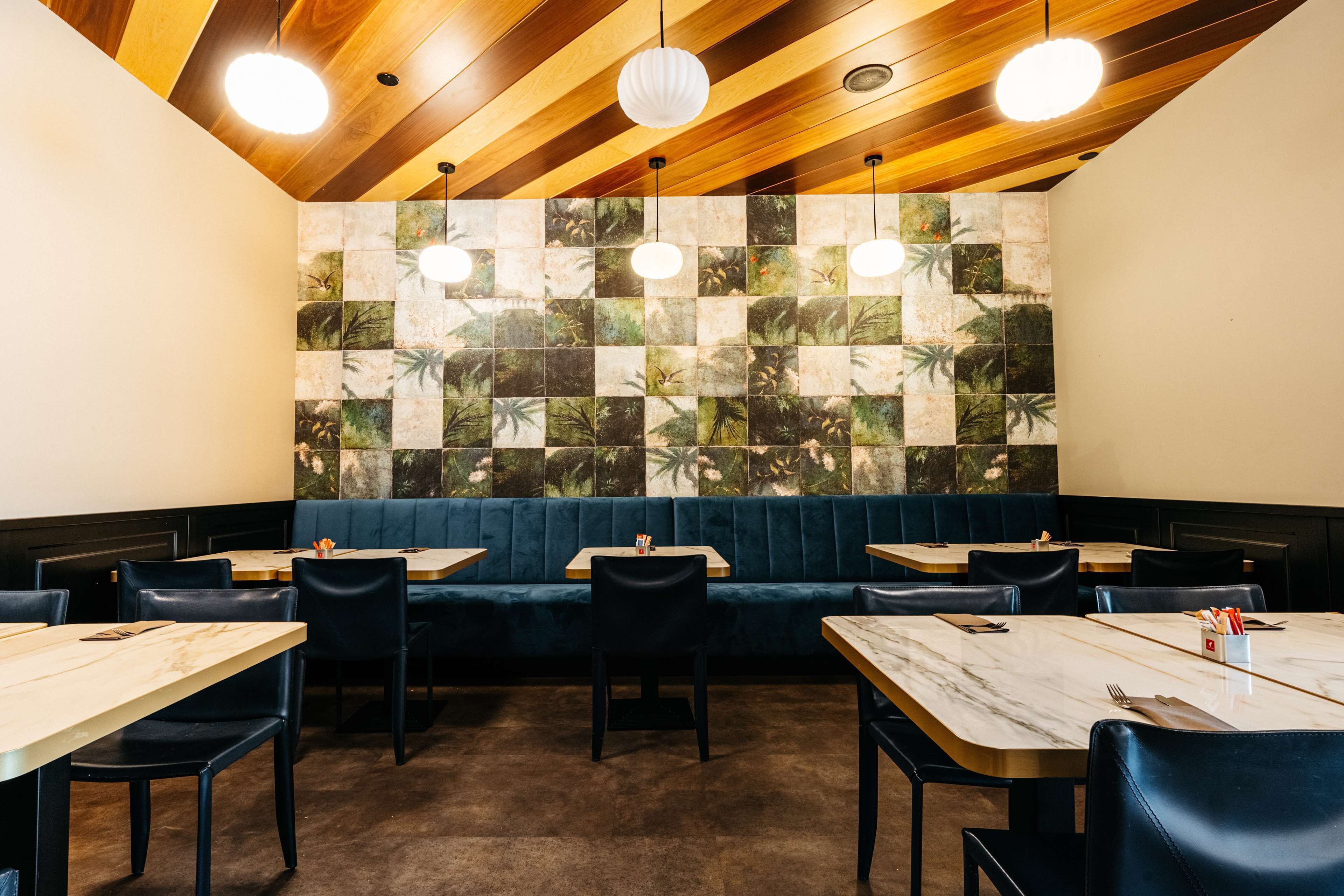 A restaurant with wooden ceiling, blue cushioned booths, and square-tiled walls.