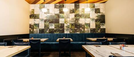 A restaurant with wooden ceiling, blue cushioned booths, and square-tiled walls.