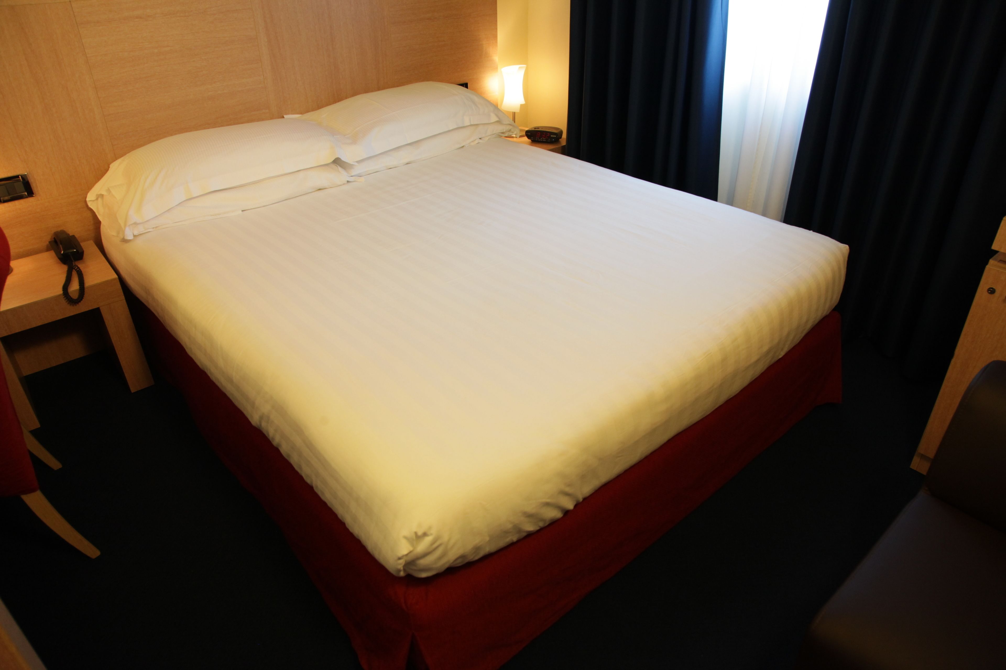 Een hotelkamer met een groot bed, een nachtkastje met een lamp en een stoel.