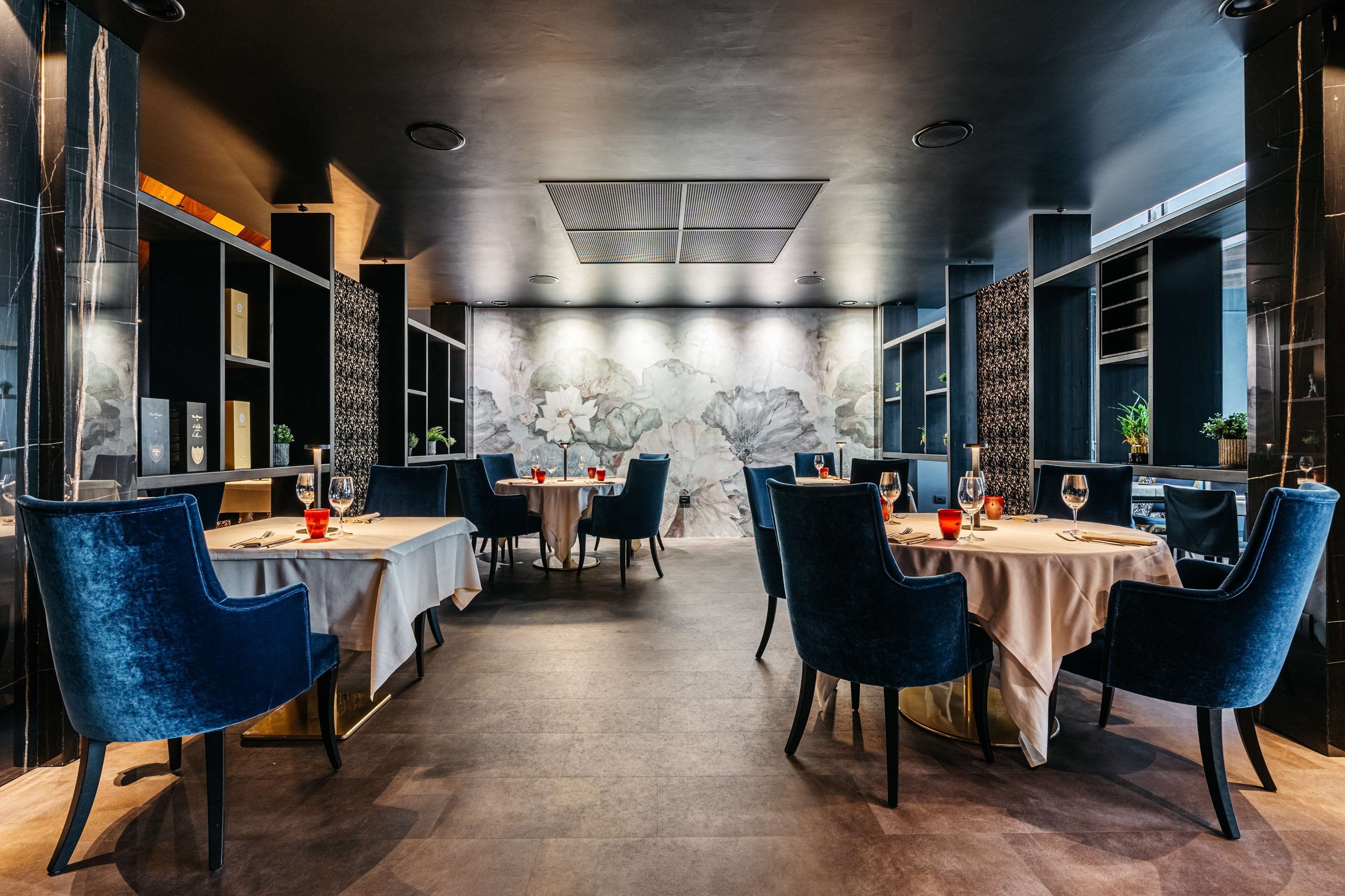 A modern dining area with tables and chairs, a decorative wall, and a ceiling light fixture.