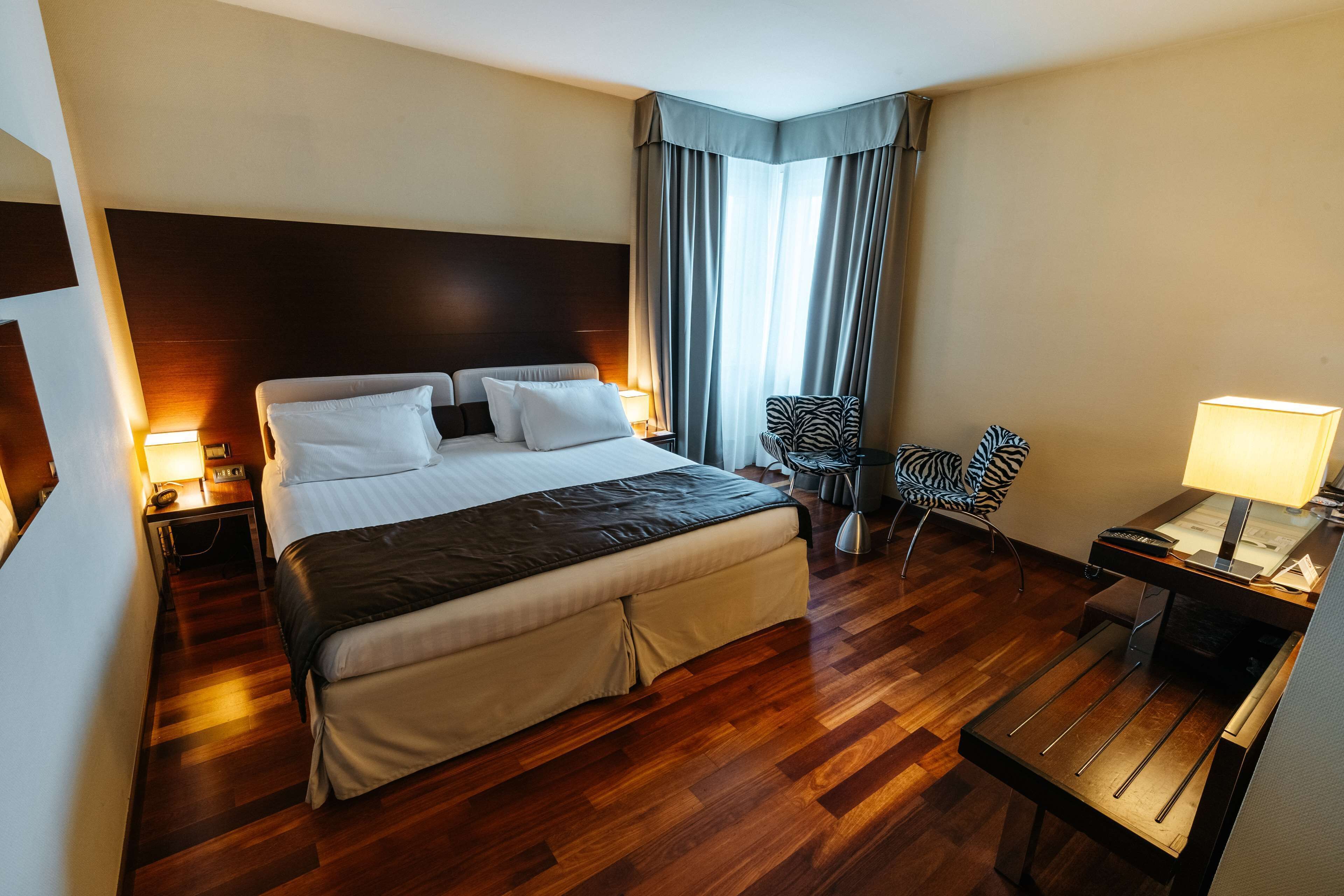 Een hotelkamer met een groot bed, een bureau, een stoel en een raam met gordijnen.