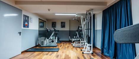 Une salle de sport équipée de matériel d’exercice, dotée d’un plancher en bois et d’un tapis de course.