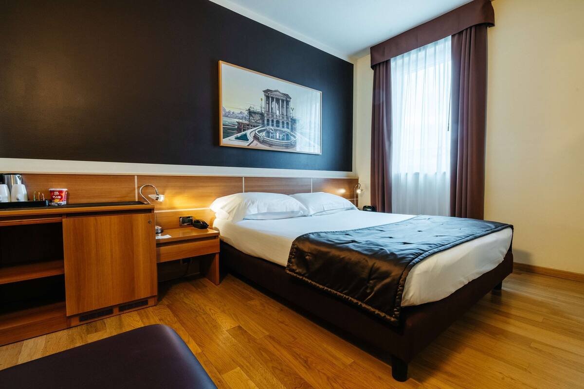 Habitación de hotel con cama, mesita de noche, lámpara y un cuadro en la pared.
