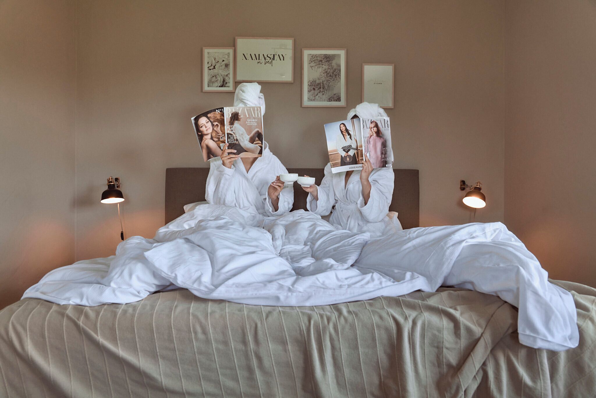 Un letto con lenzuola bianche e una coperta a righe, due abat-jour e quadri appesi al muro.
