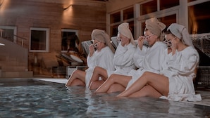 A group of people in white robes sitting by a pool in a wooden room with large windows. - MANA LISA Boutiquehotel (Lauda)