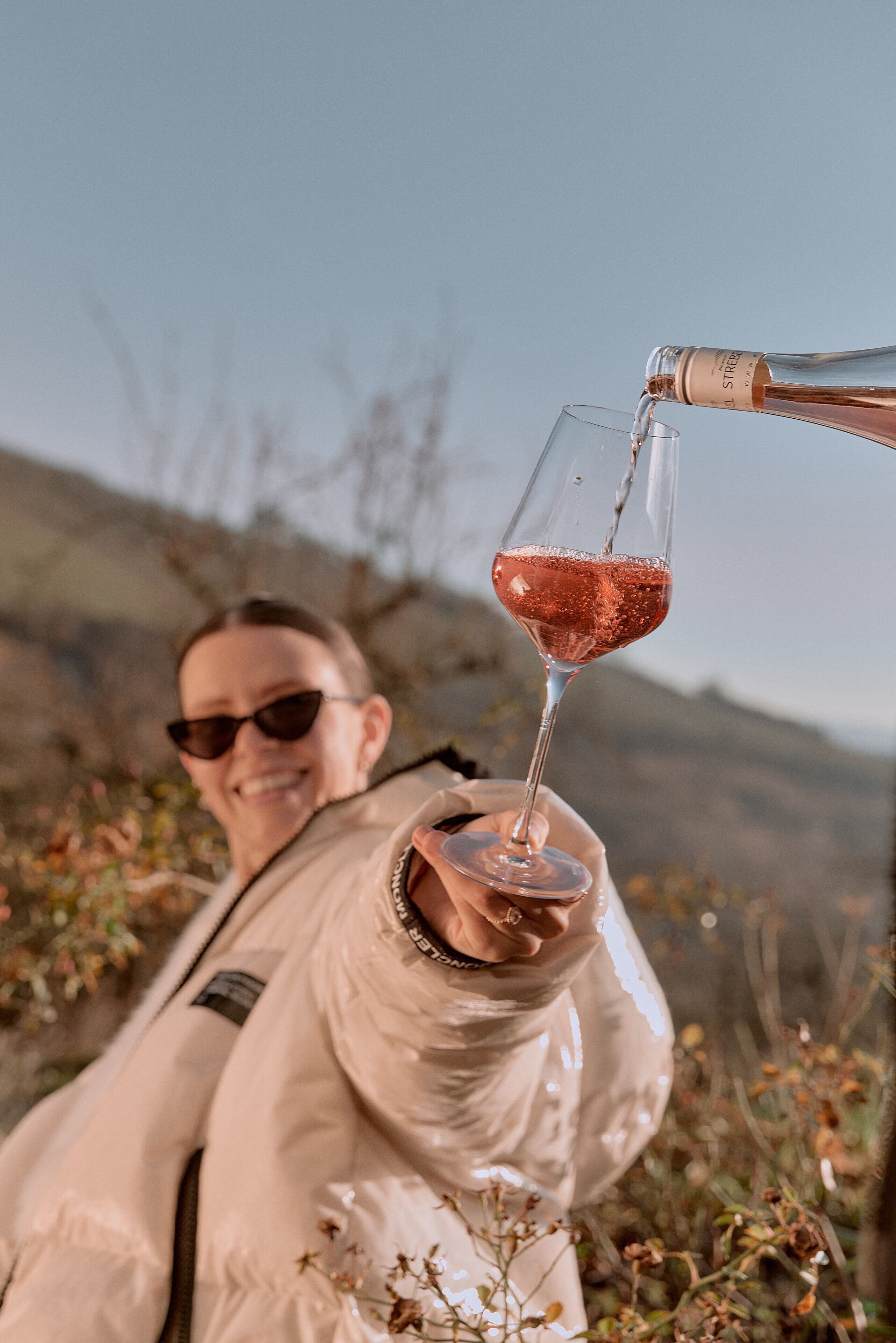 Eine Person hält ein Weinglas, in das eine Flasche eingegossen wird.