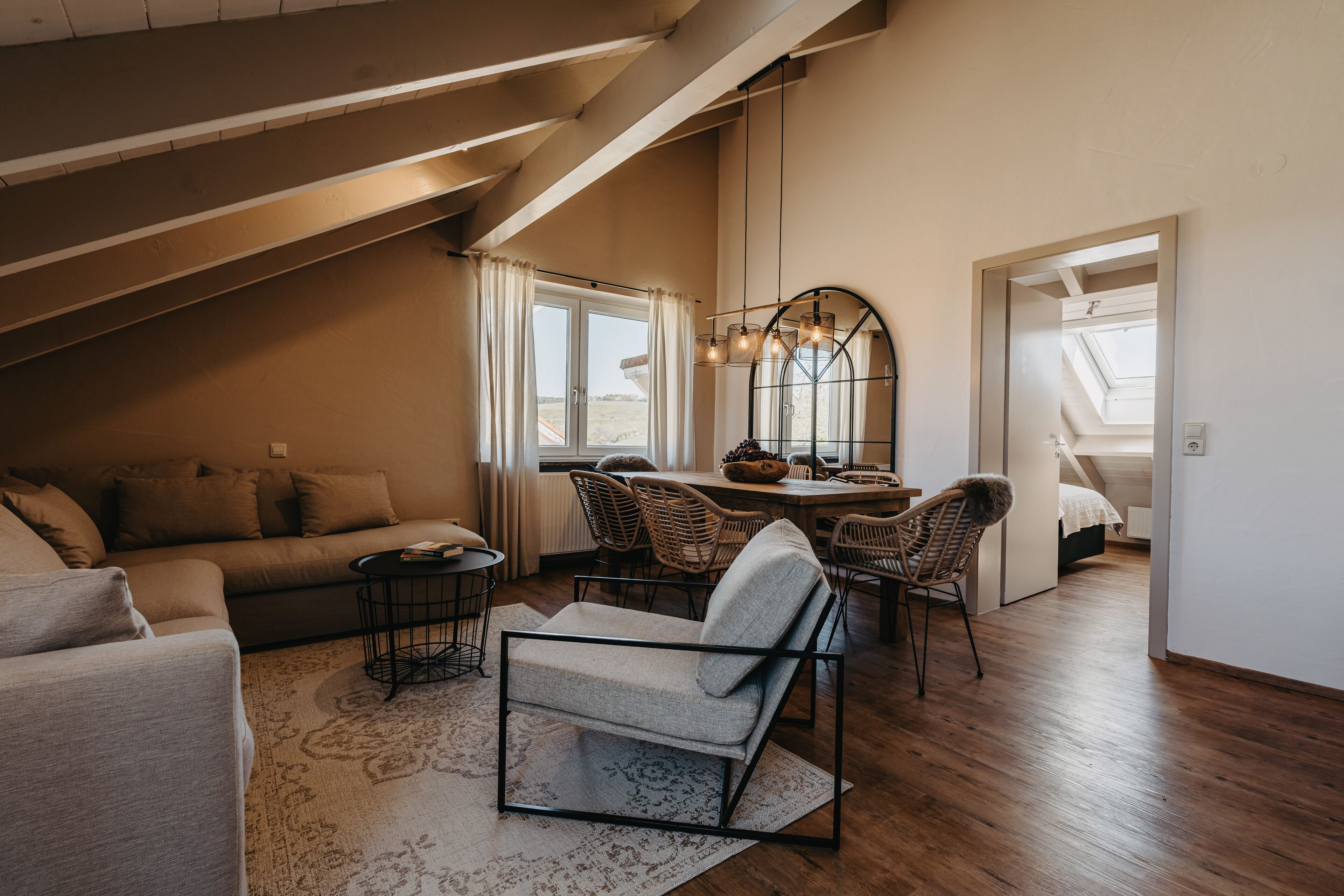 A cozy loft bedroom with a sloped ceiling, a dining area with wicker chairs, and a large window providing natural light.