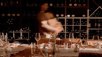 A dining table set with wine glasses, plates, and cutlery, with a wine rack in the background.