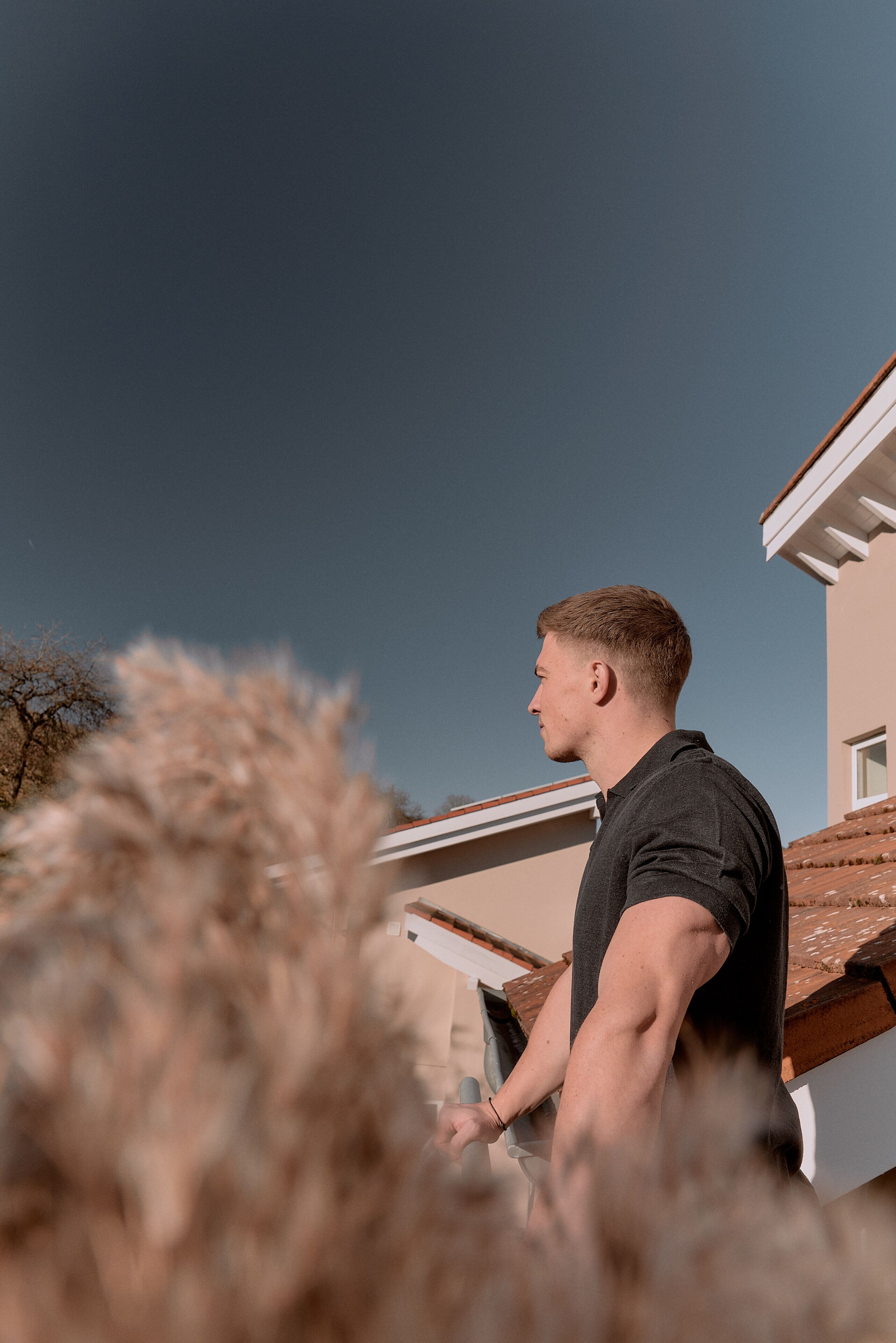 A person standing on a roof, overlooking a house with a sloped roof and a clear sky.