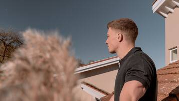 A person standing on a roof, overlooking a house with a sloped roof and a clear sky.