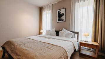 Una cama bien hecha con un edredón color beige, una mesita de noche con una lámpara y un cuadro en la pared.