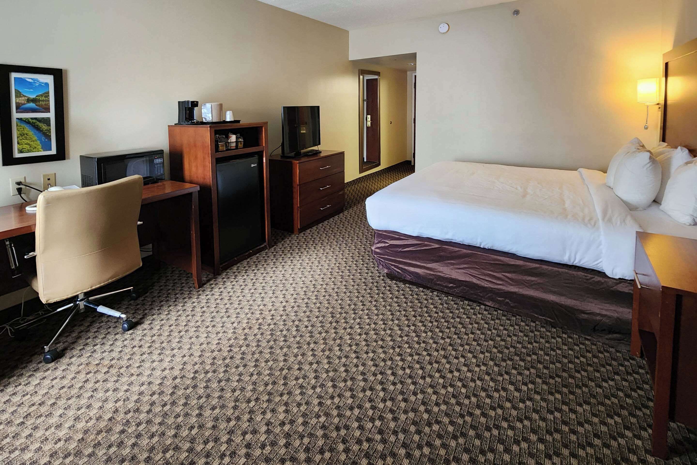 A hotel room with a bed, a desk with a computer, a television, and a mirror.