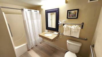 A bathroom with a shower, a sink with a mirror, a toilet, and towels on a rack.