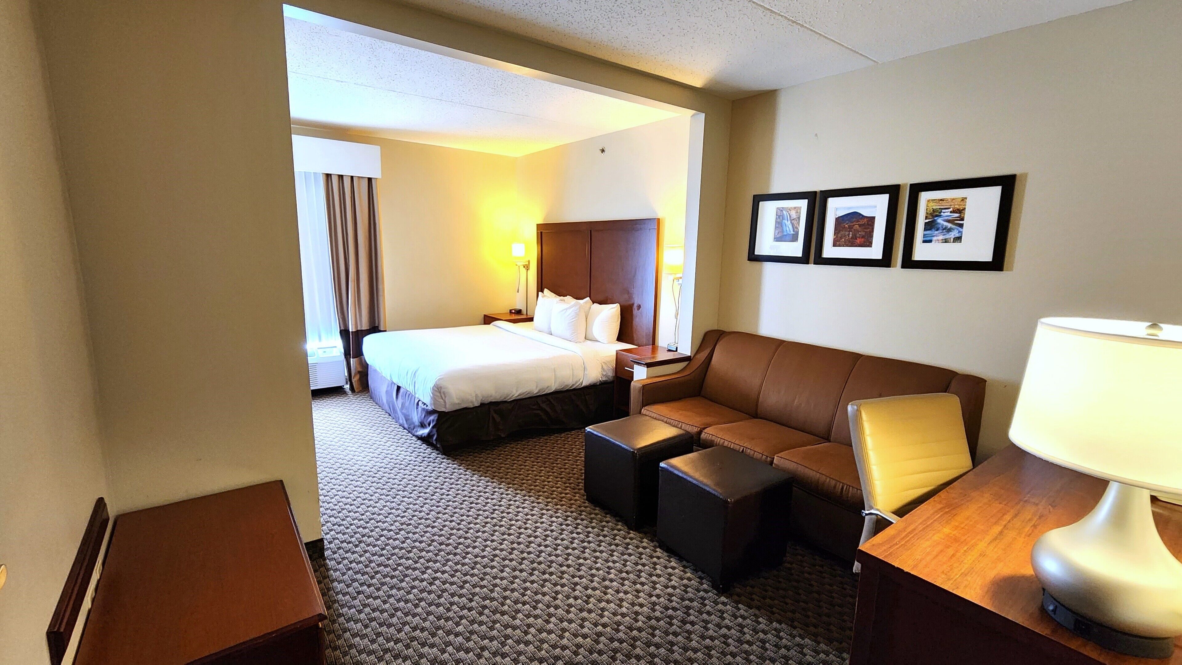 Een hotelkamer met een bed, een bank, een bureau met een lamp en drie ingelijste foto’s aan de muur.