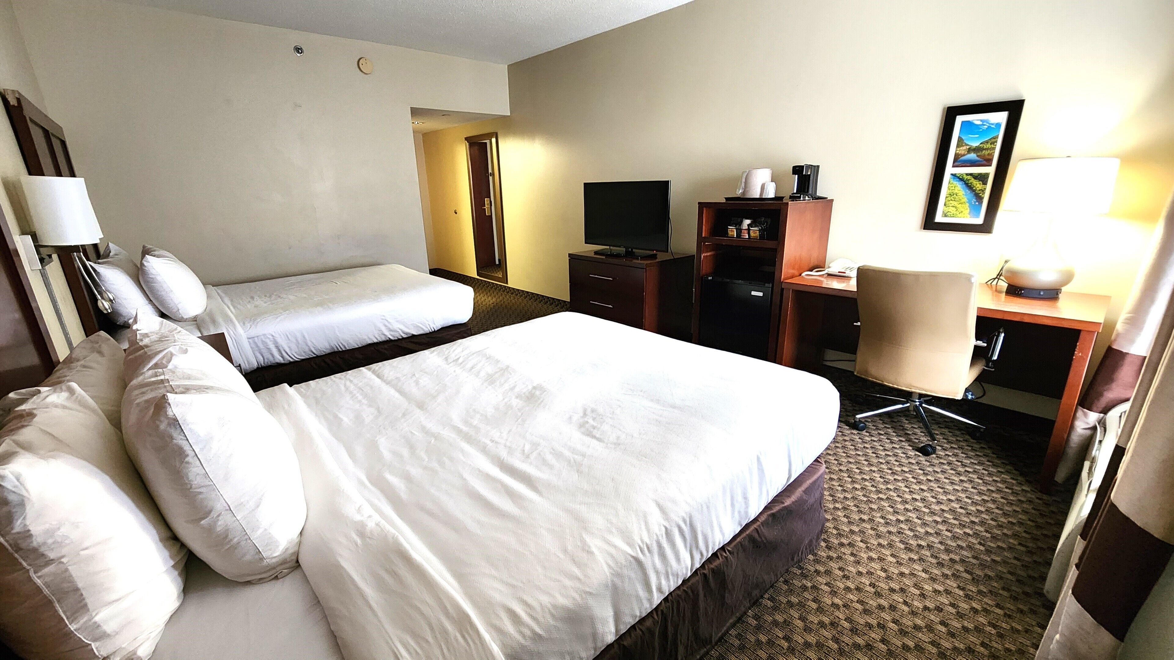 A hotel room with two beds, a desk, a chair, a television, and a lamp.